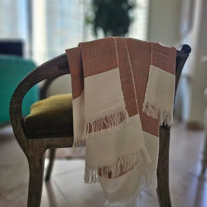 Lomyna LOVE orange towel with diamond weave pattern placed on the arm of a chair.