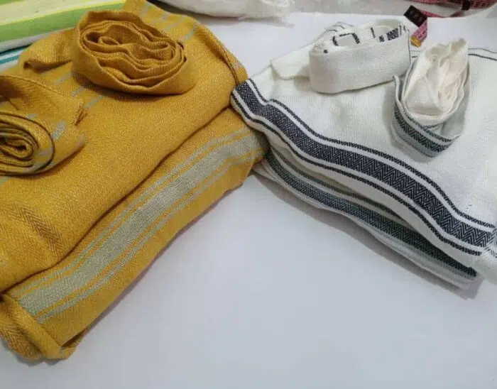 Two folded Lomyna LOBA robe luxury viscode or cotton towels in white and mustard color, neatly stacked in a minimal composition.
