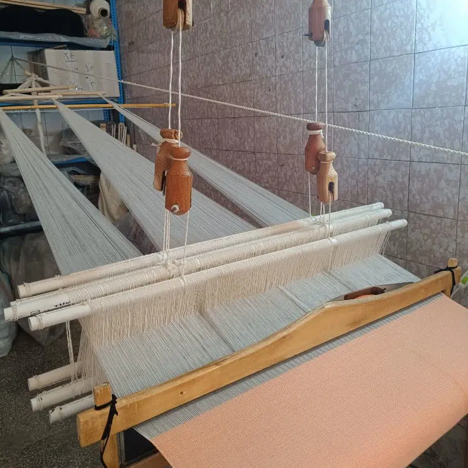 Wooden weaving loom with a handwoven towel in progress, showing an orange Lomyna Love towel on the loom.