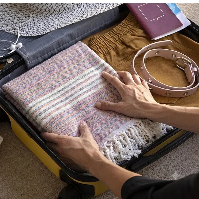 "A hand-woven Lumina towel with delicate texture and soft colors, perfectly packed in a suitcase for a luxurious and lightweight travel experience."